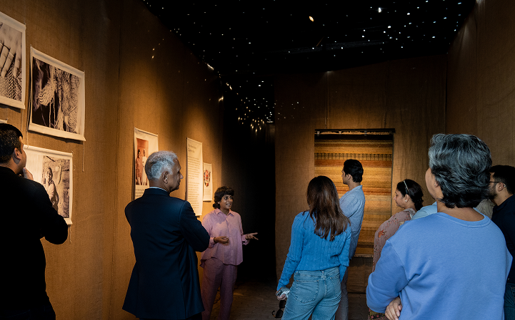 Visitors in a craft and textile exhibition room lit low